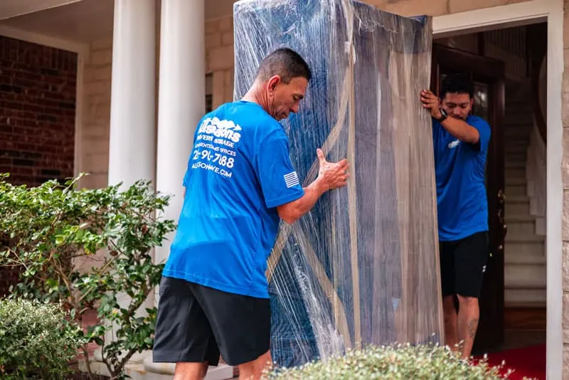 Movers carrying wrapped furniture out of a Sugar Land home