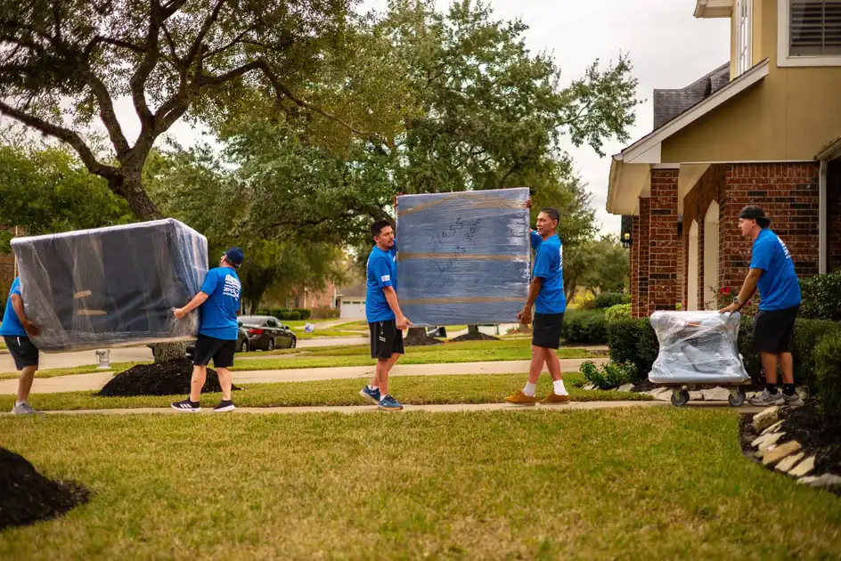 Movers carrying wrapped furniture across a front lawn in Sugar Land, TX
