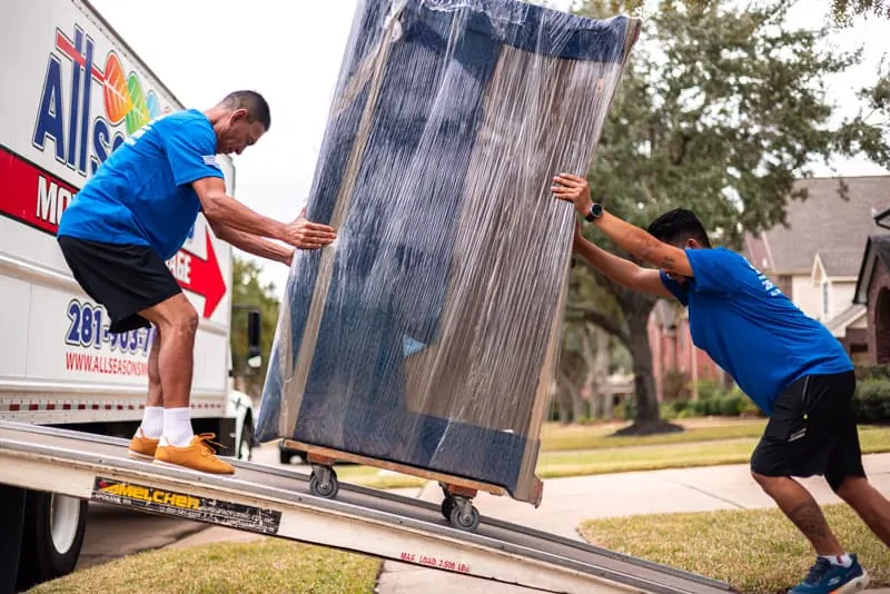 Movers pushing wrapped furniture up the truck ramp in Sugar Land