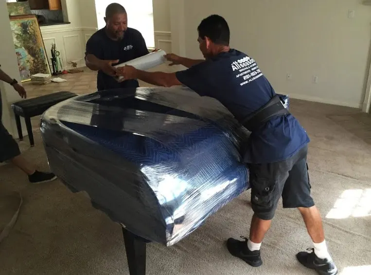 Piano movers moving a wrapped grand piano in Sugar Land, TX